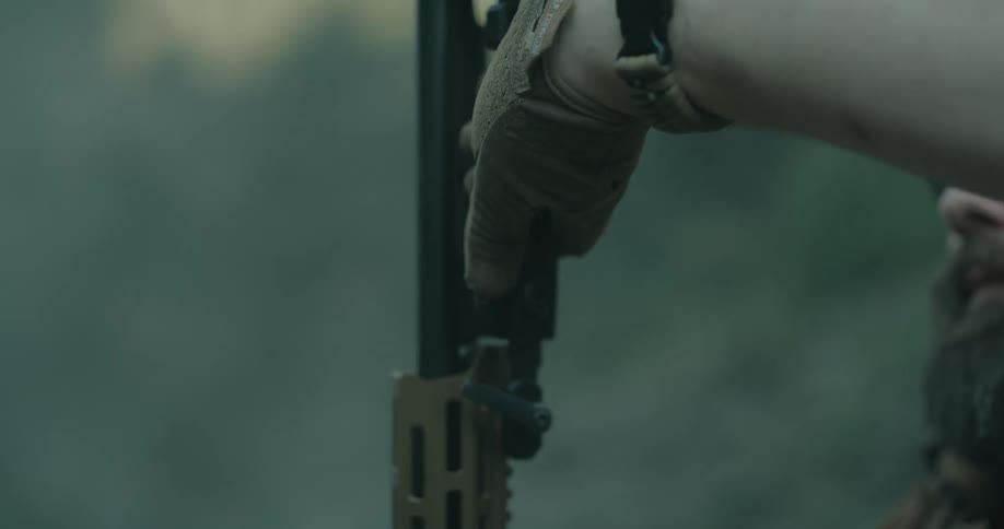 A hunter readies a large weapon as he sits in the forest