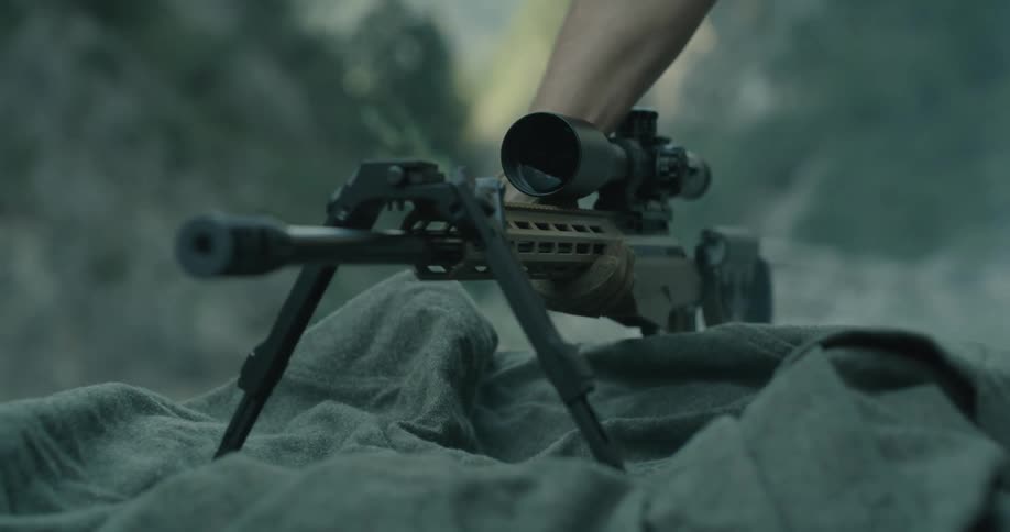 A person with gloves putting down a rifle with a scope with cliffs in the background