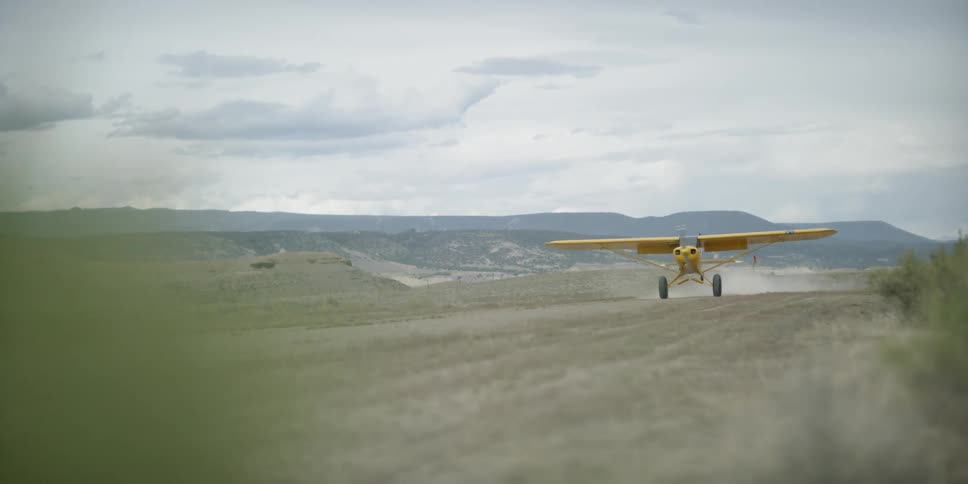 A yellow plane lands on a dirt runway