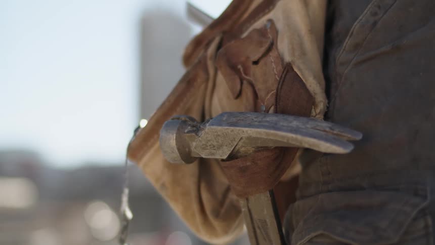A construction worker standing with a hammer in a toolbelt on a worksite