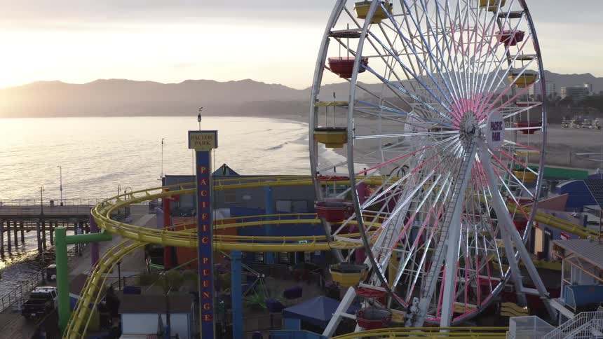 A ferris wheel looms above a beach amusement park next to the ocean and near downtown