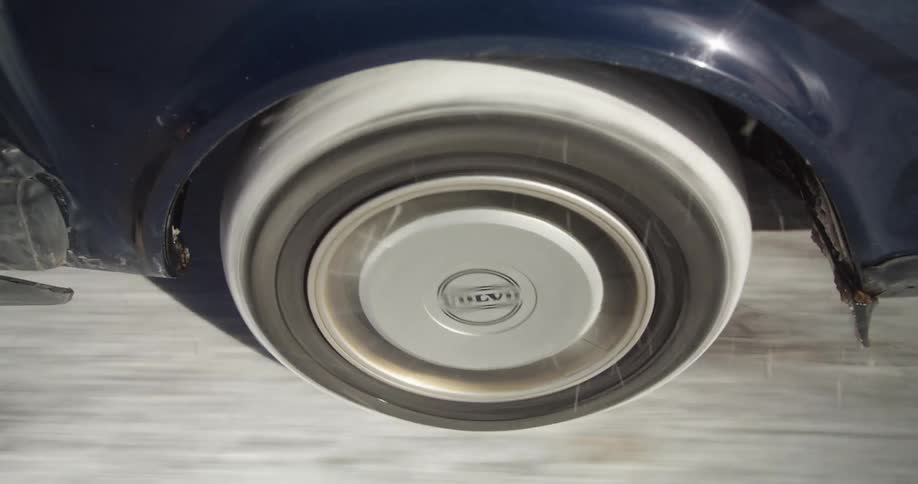 Snow packs onto the tire of a blue vehicle as it drives along a road packed with ice and snow