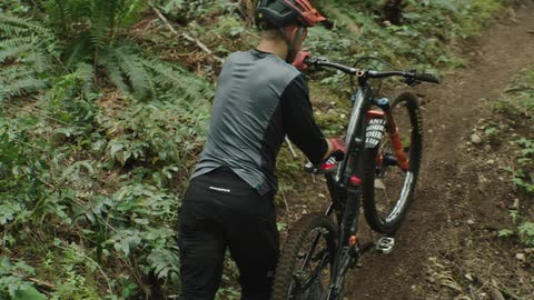A man with a helmet and gloves pushing a bike on a pathway in the forest