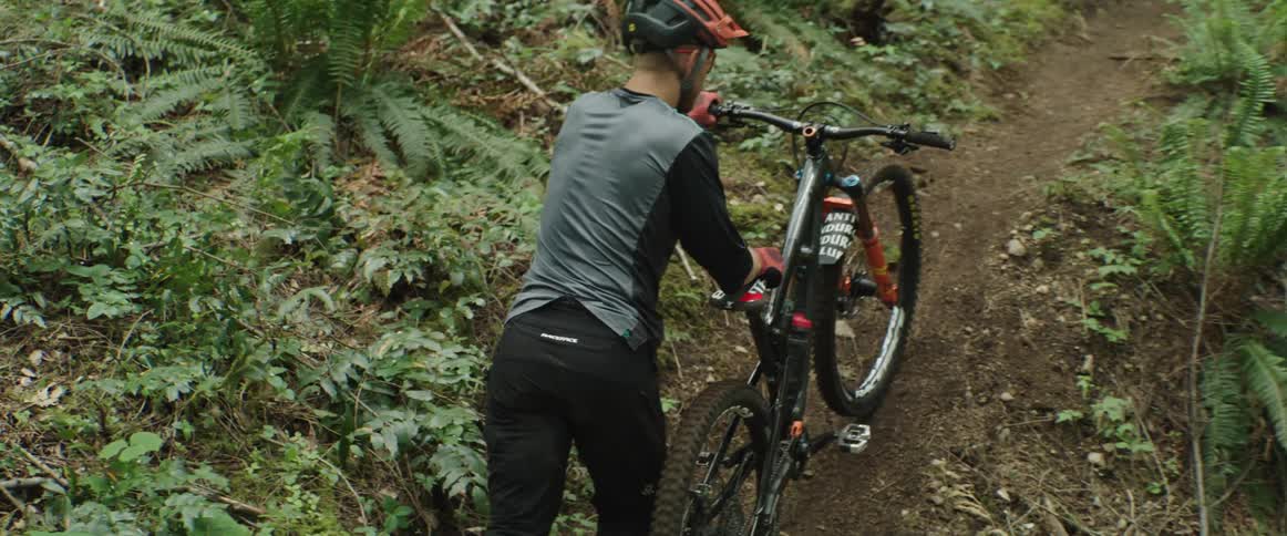 A man with a helmet and gloves pushing a bike on a pathway in the forest