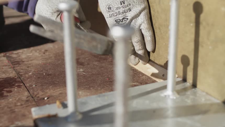 A person wearing workers gloves hammers a nail into a building during the day