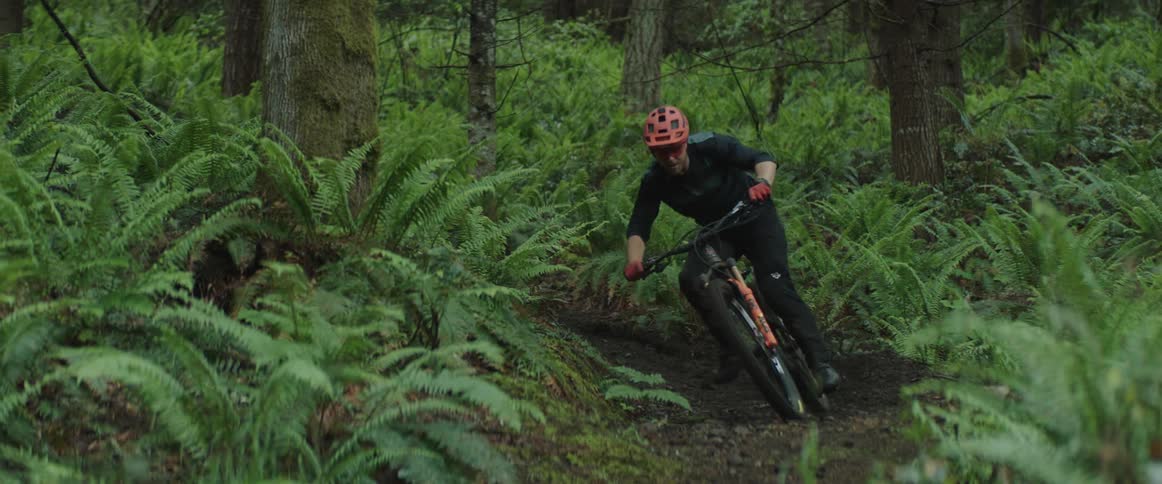 A man with a helmet and gloves riding a bike through a muddy rut in a forest