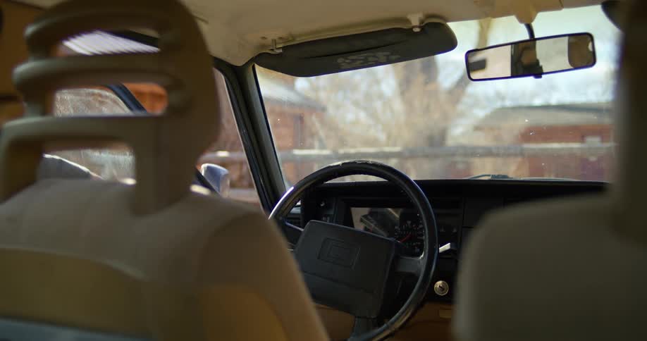 A woman exits the drivers seat of a vehicle and walks towards a building during the day