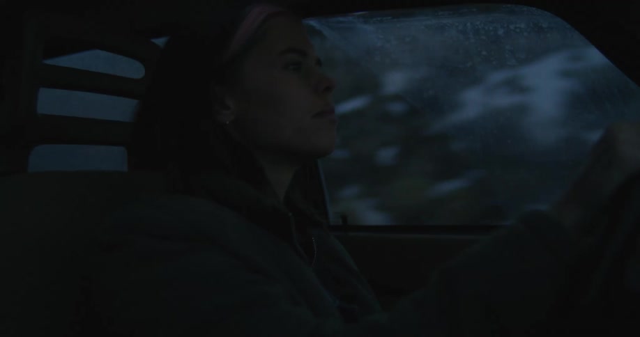 A woman in a vehicle driving and turning the steering wheel with the sky and clouds in the background