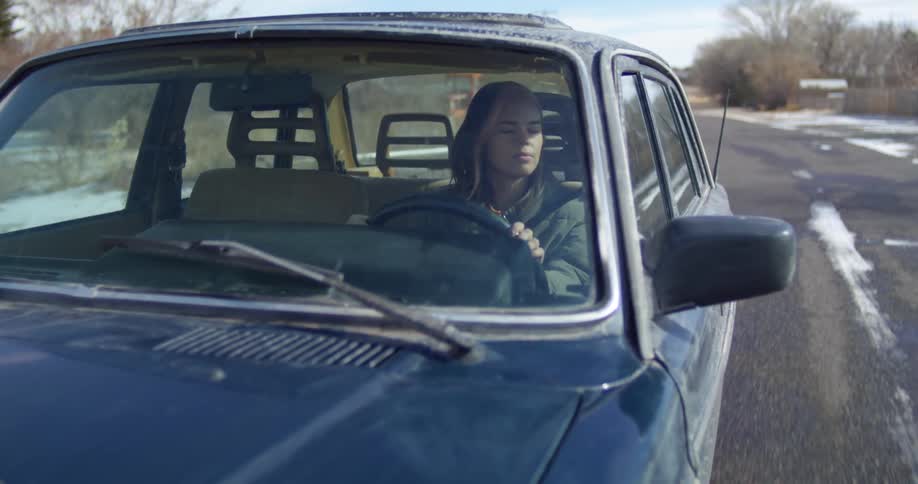 A young woman looks back and forth as she drives along a snow covered rural road