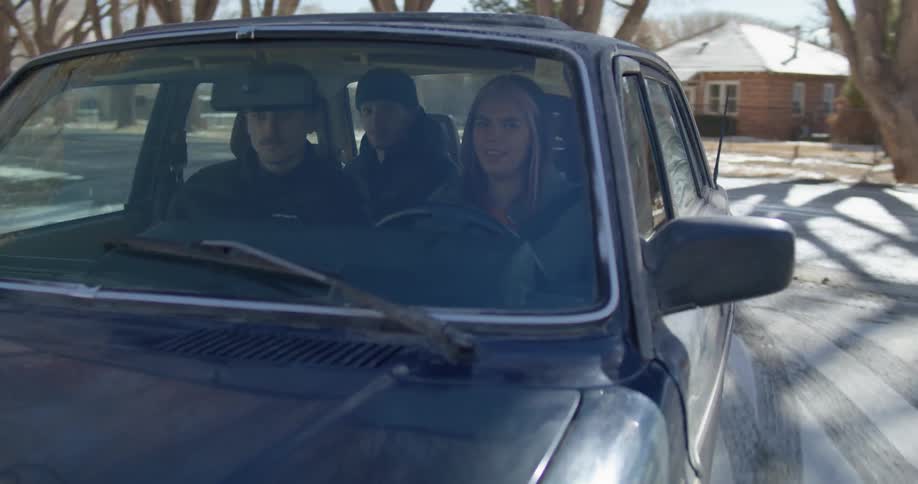 Woman wearing a hoodie driving a car with her friends on a rural road at daytime