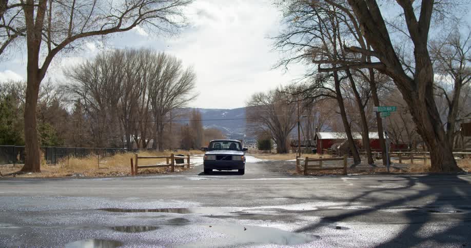 A vehicle driving on a road with trees the sky and clouds in the background