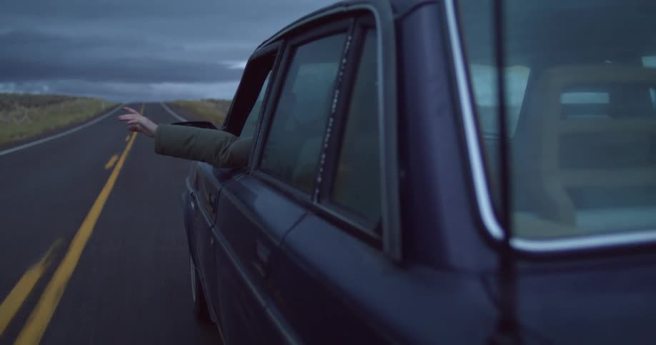 Woman driving a car on a rural road waves her hand outside the drivers window at daytime