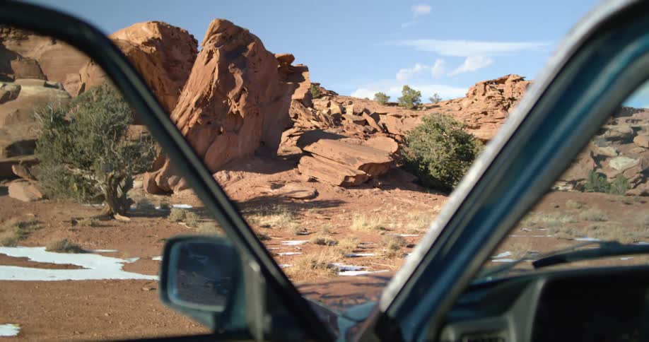 A vehicle with a rearview mirror and a steering wheel with a landscape the sky and clouds in the background