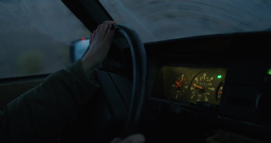 A woman drives down a rural highway at dusk