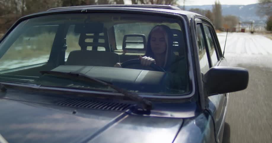 Woman wearing a hoodie driving a car on a rural road at daytime