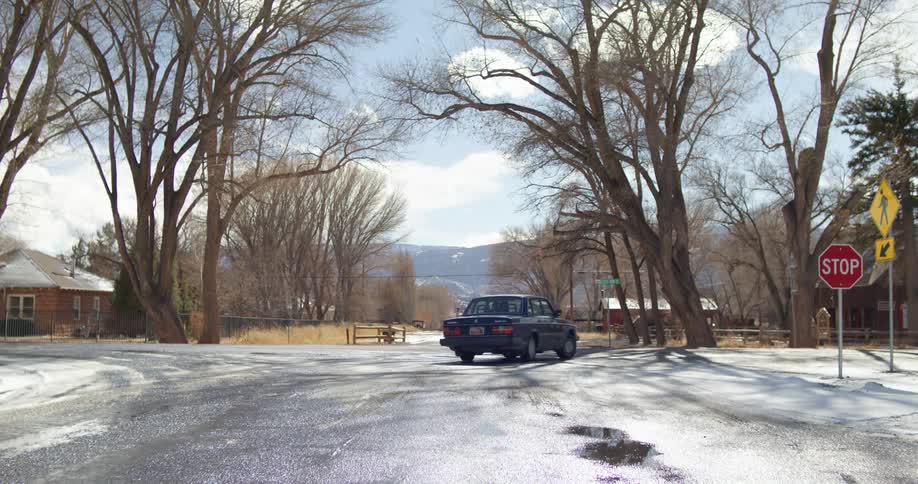Car turns corner on road in neighborhood covered with snow with mountains on horizon