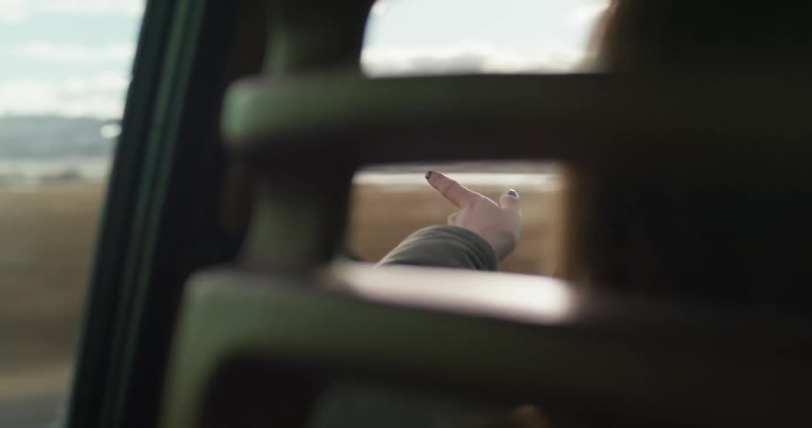 Woman driving a car on a rural road waves her hand outside the dirvers window at daytime