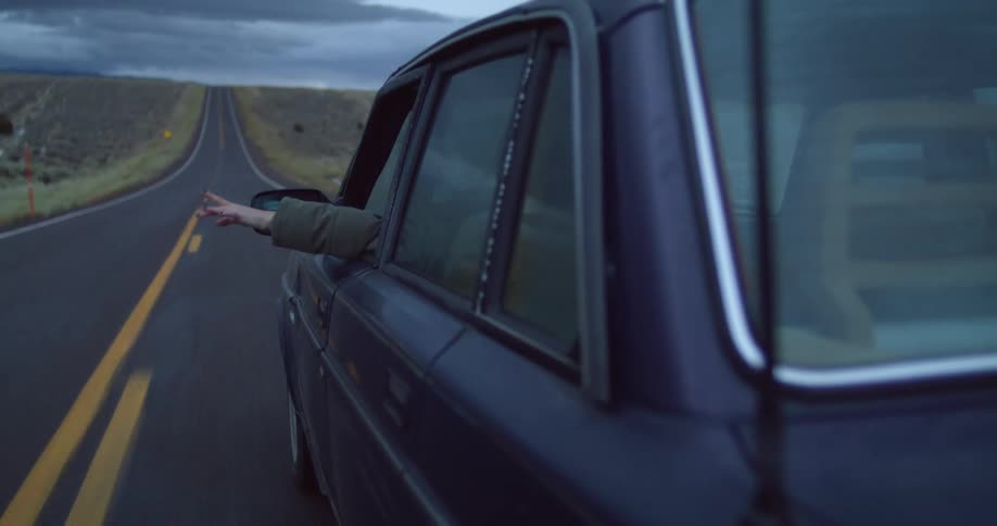 A person driving a vehicle with their hand out the window with the sky and clouds in the background