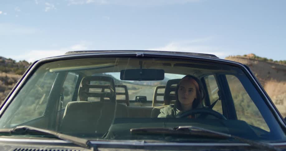 Woman wearing a hoodie driving a car on a rural road at daytime