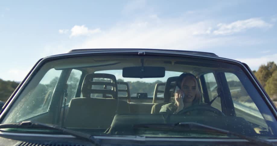 A woman driving a vehicle and talking on a smart phone with the sky and clouds in the background