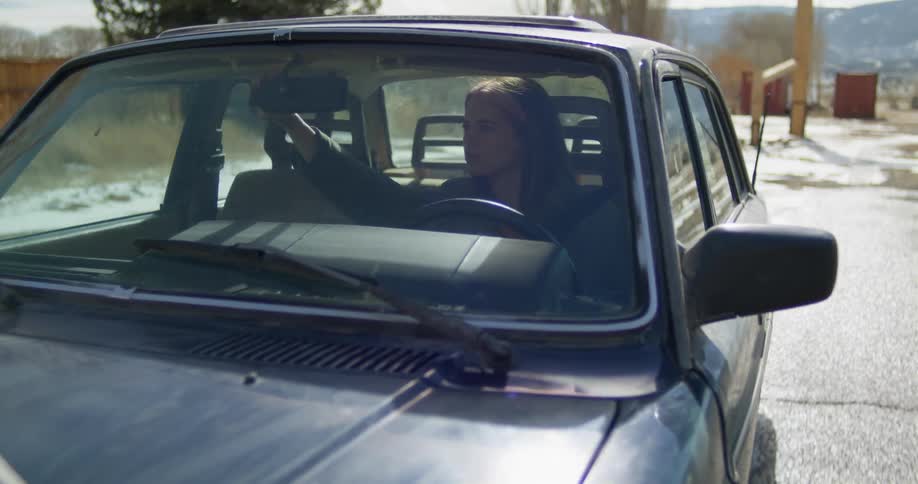 A young woman adjusts the rearview mirror of a car as she begins to accelerate