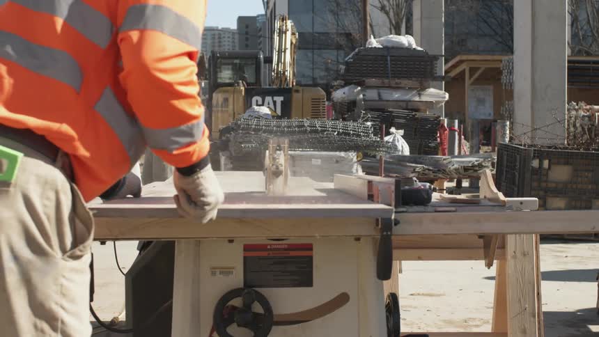 A construction worker uses a table saw outdoors to cut a piece of wood at a construction site