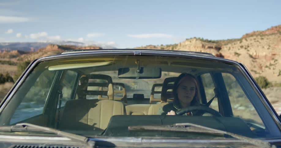 A woman driving a vehicle and turning the steering wheel with the sky and clouds in the background