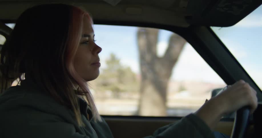 A woman drives a vehicle through a rural area during the day