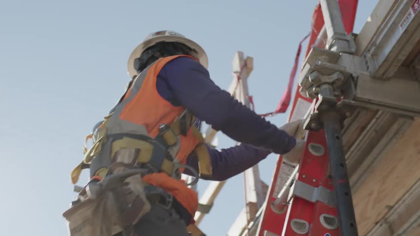 Construction worker wearing hardhat tool belt and vest climbs ladder