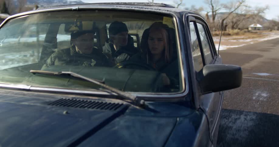 A woman driving a car on small town road with two passengers in the vehicle