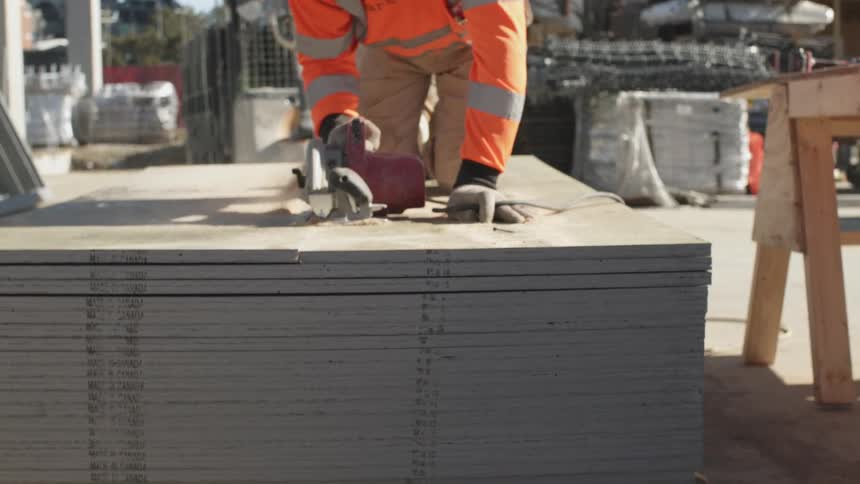 A person with gloves cutting pieces of wood with an electrical saw in a construction site