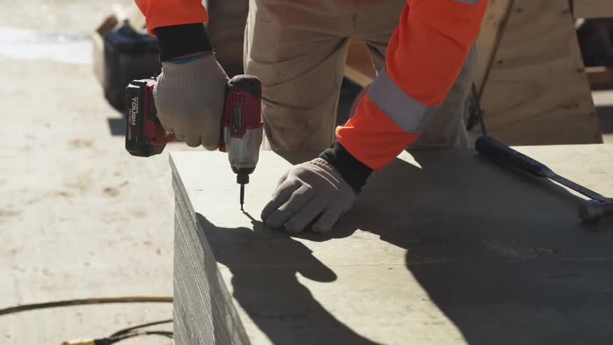 Laborer uses battery powered electric screwdriver to drive screw in large box outside