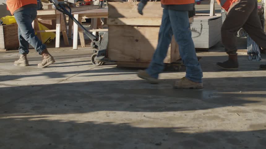 Construction workers in orange vests hauling supplies at a worksite