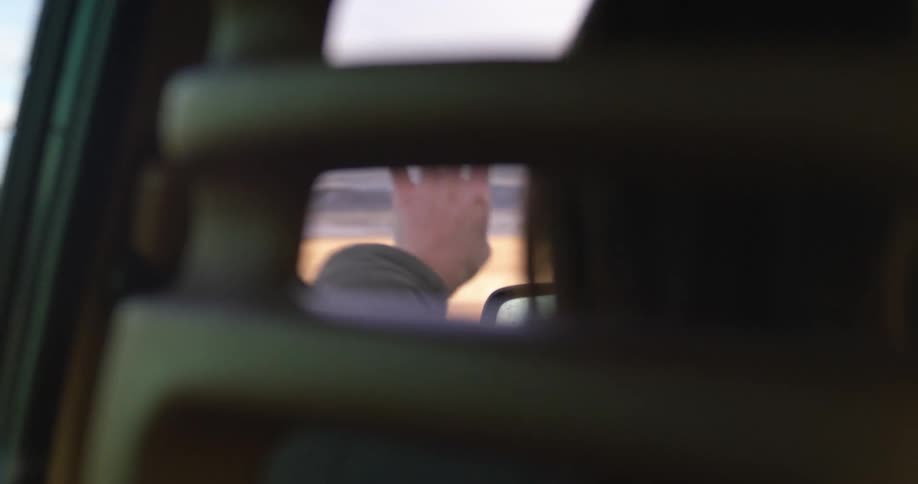 Woman driving a car on a rural road waves her hand outside the dirvers window at daytime