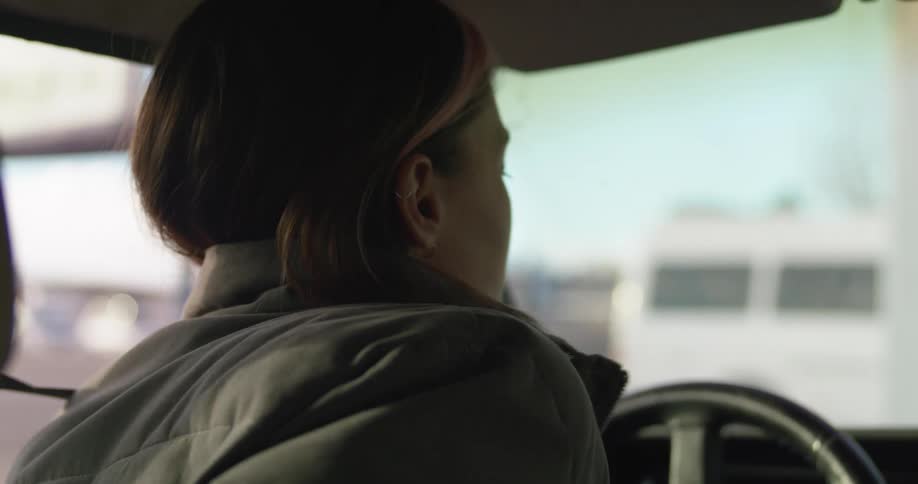 A woman in a green jacket unbuckles her seat belt and gets out the front seat of her vehicle