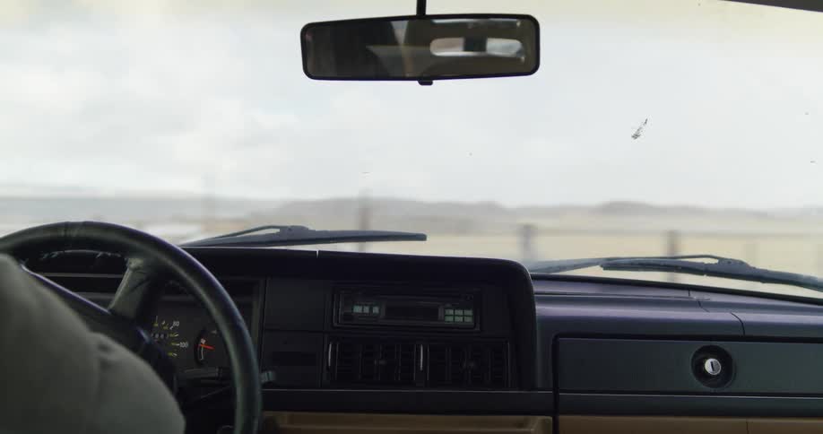 A woman driving a vehicle and turning the steering wheel with the sky and clouds in the background