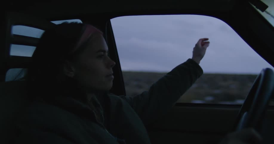 Woman driving a car on a rural road waves her hand outside the dirvers window at morning