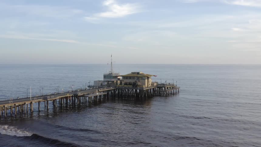 Aerial view of a building at the end of a dock next to the coast over the ocean in the evening