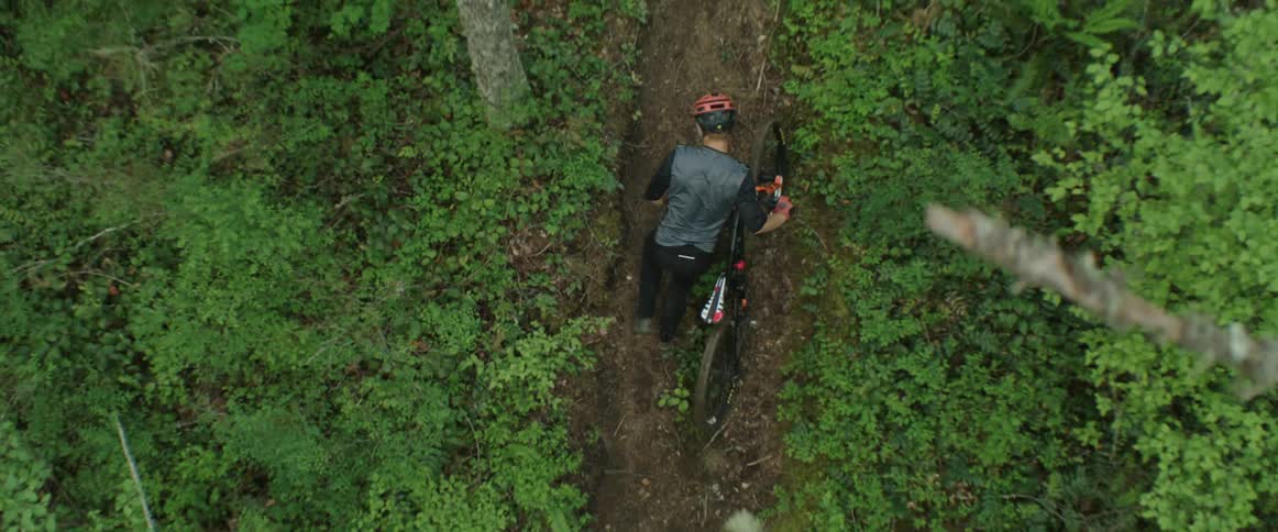 A man pushing a mountain bike up a dirt trail in a forested area