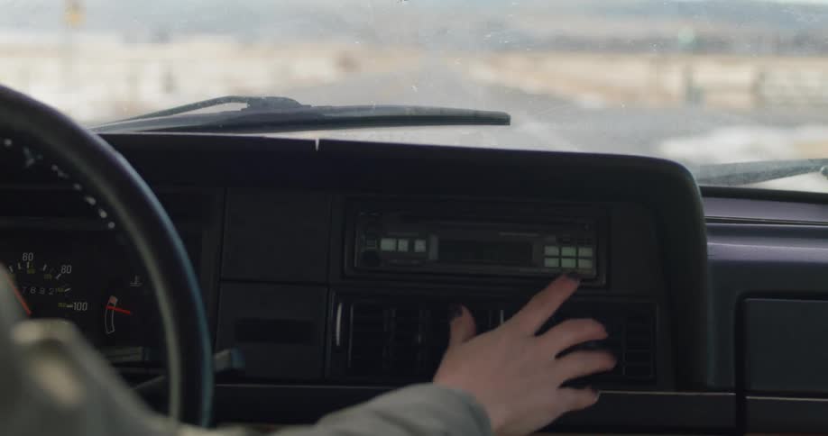 Blonde woman adjust setting on dashboard as she drives car through snowy countryside toward mountains