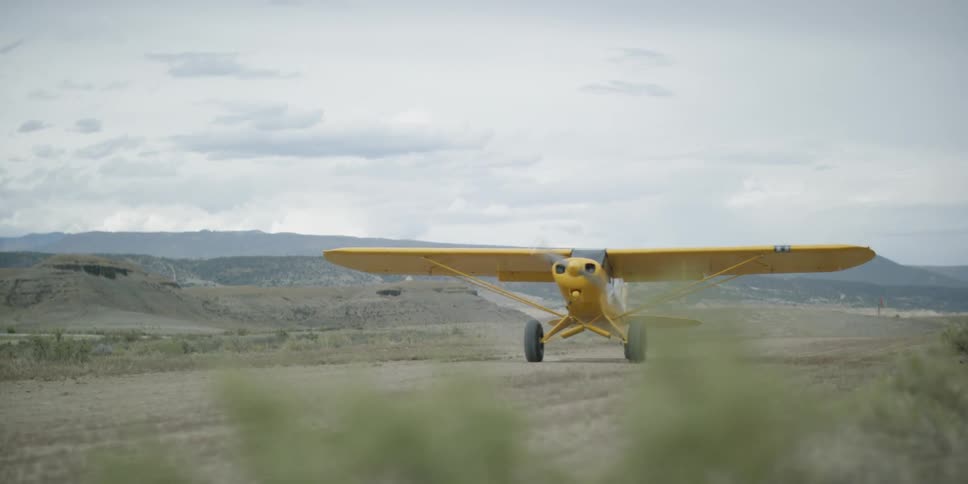 A yellow plane lands on a dirt runway