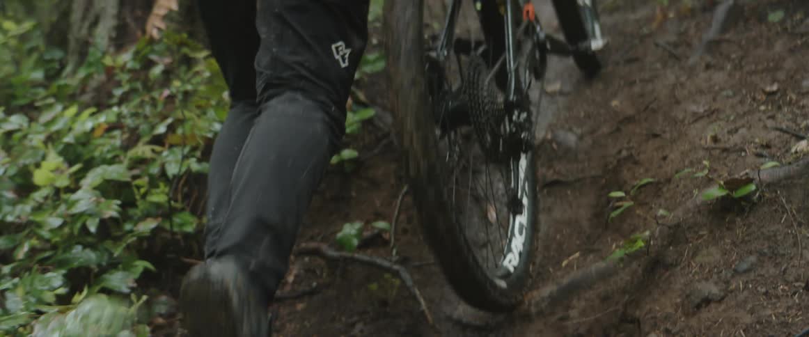 A person pushing a bike on a muddy path in a forest