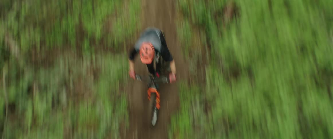 Man rides mountain bike rapidly down dirt path through forest