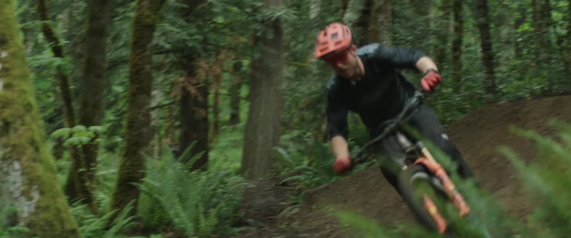 A cyclist is sent airborne while biking at high speed through a forest during the day