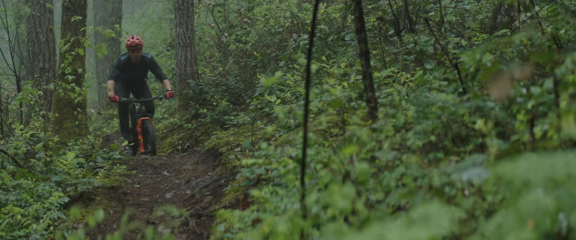 A man riding a mountain bike kicks out his tire on a dirt trail in a forest