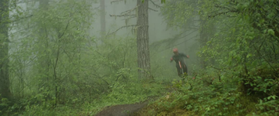 A man whips a mountain bike over a jump in a foggy forest