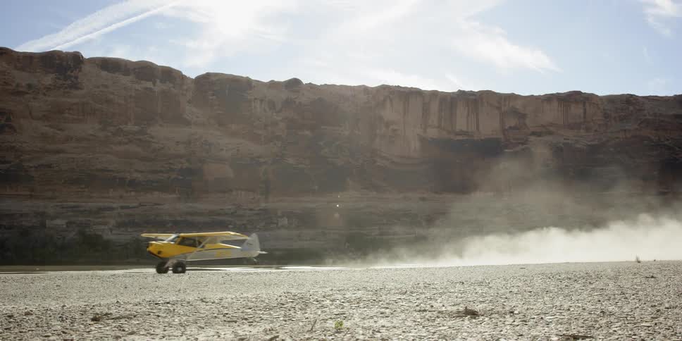 A small yellow airplane takes off in a desert