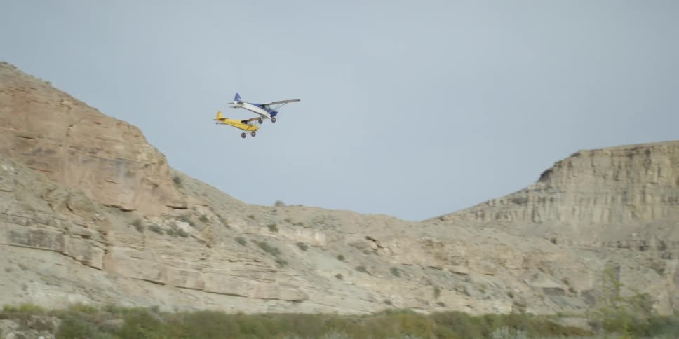 Two small airplanes fly together beside  a rock formation