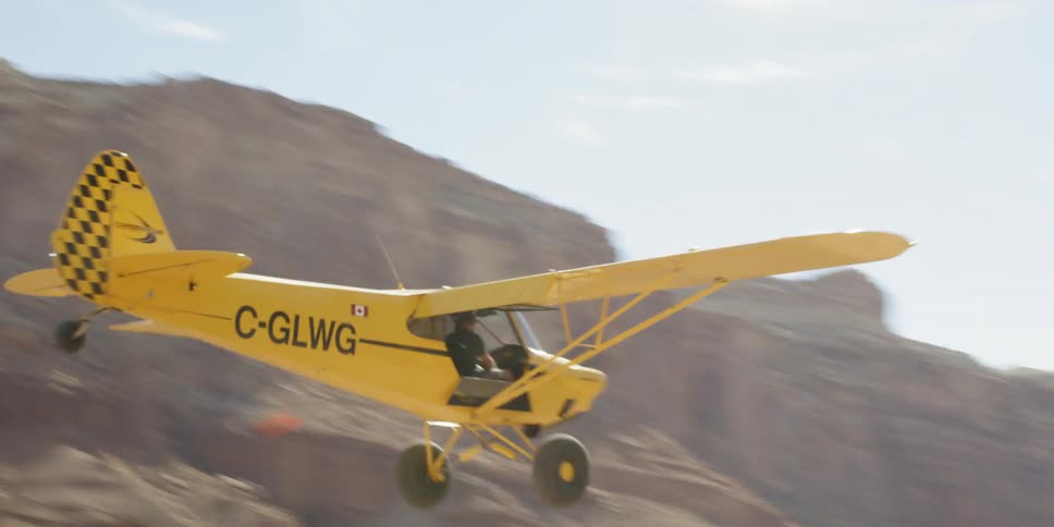 A yellow plane landing on a dirt runway