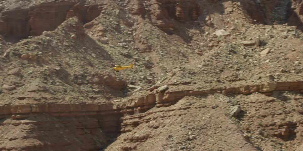 A small yellow airplane takes off over a desert